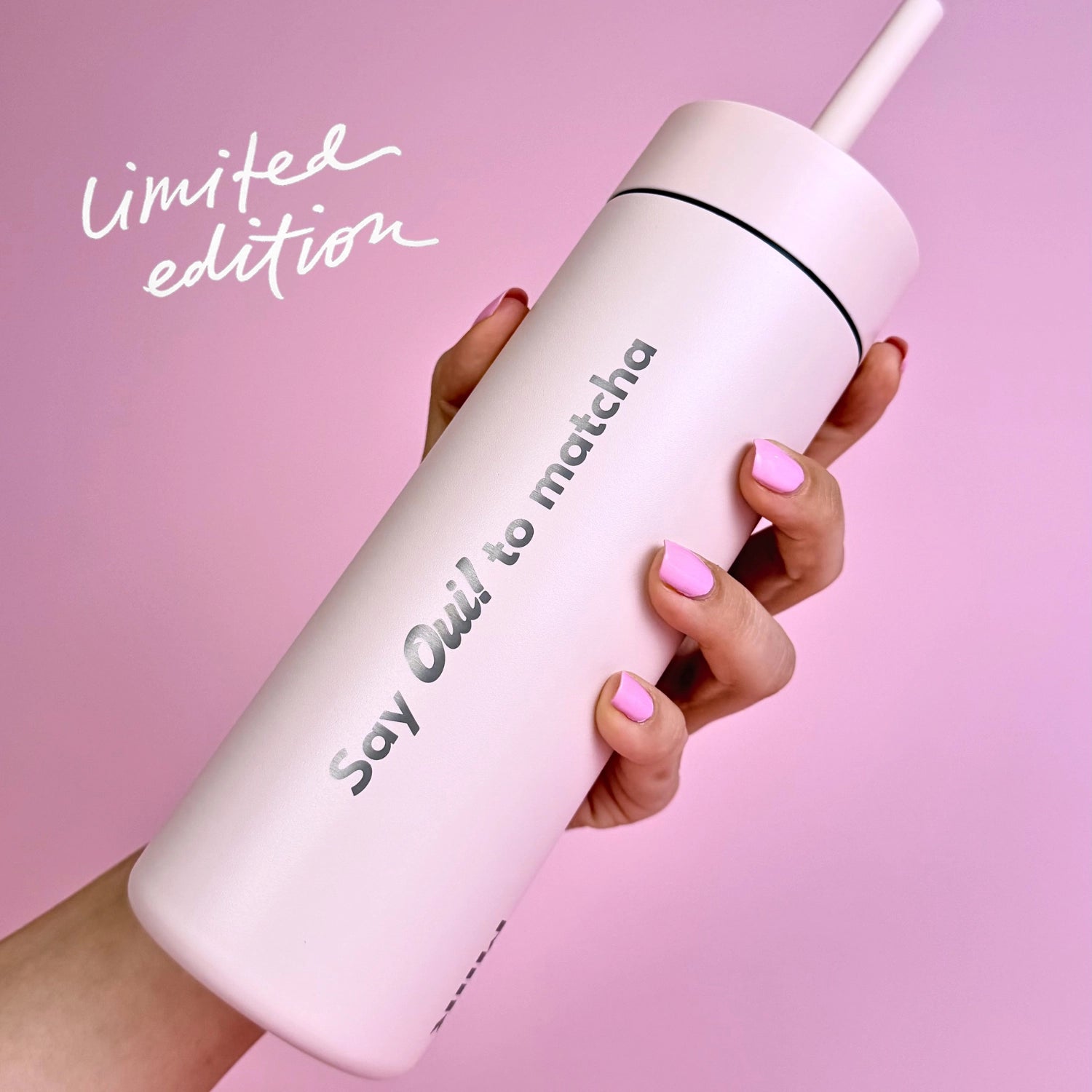 Hand holding a 'Ouatcha Matcha' tumbler with a straw on a pink background