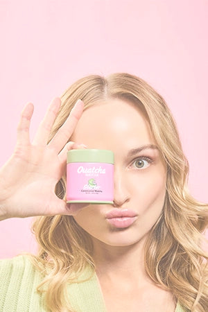 Woman holding a pink Ouatcha Matcha tin with a green lid against a pink background.