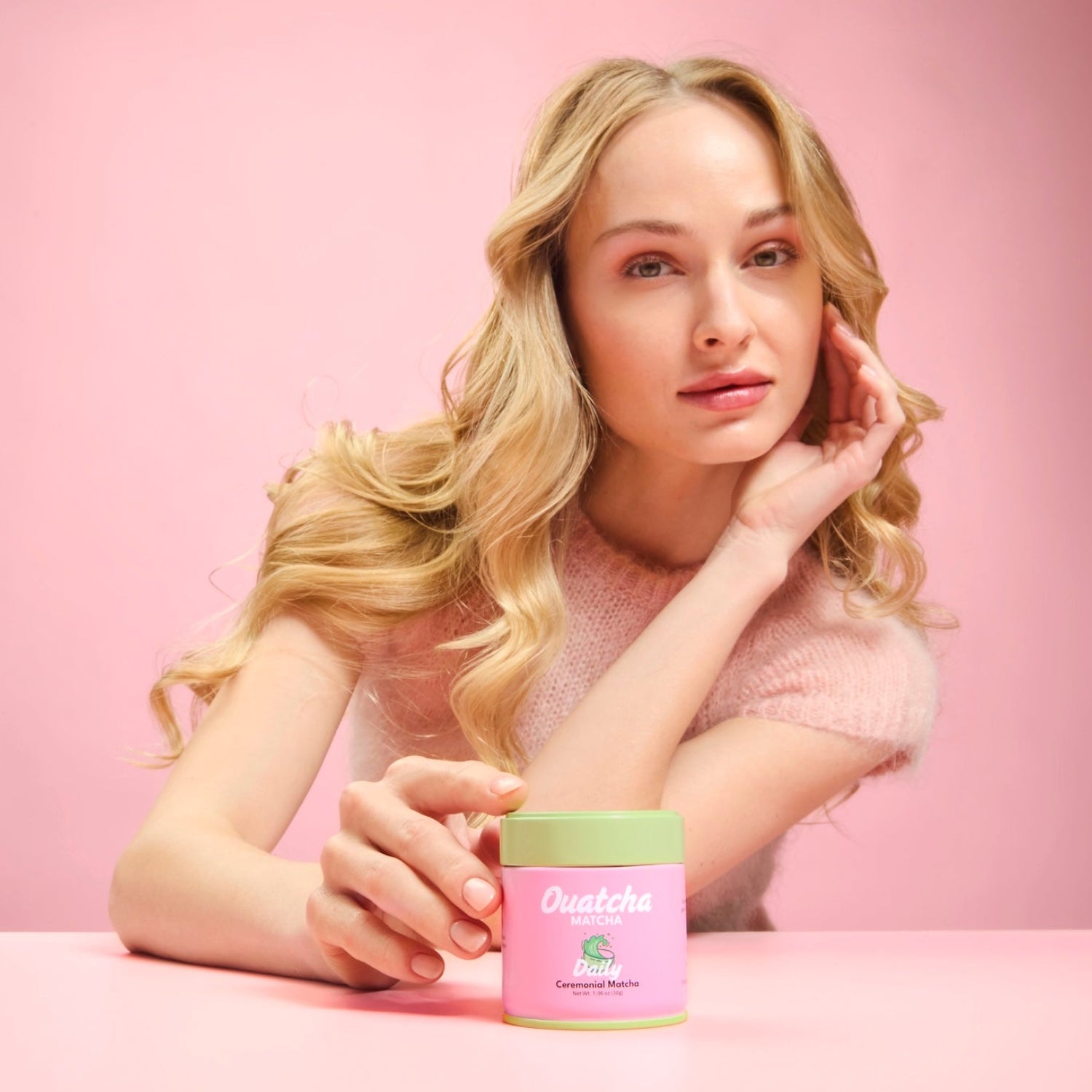 Woman holding a Daily Ouatcha Matcha ceremonial-grade first harvest matcha tin against a soft pink background