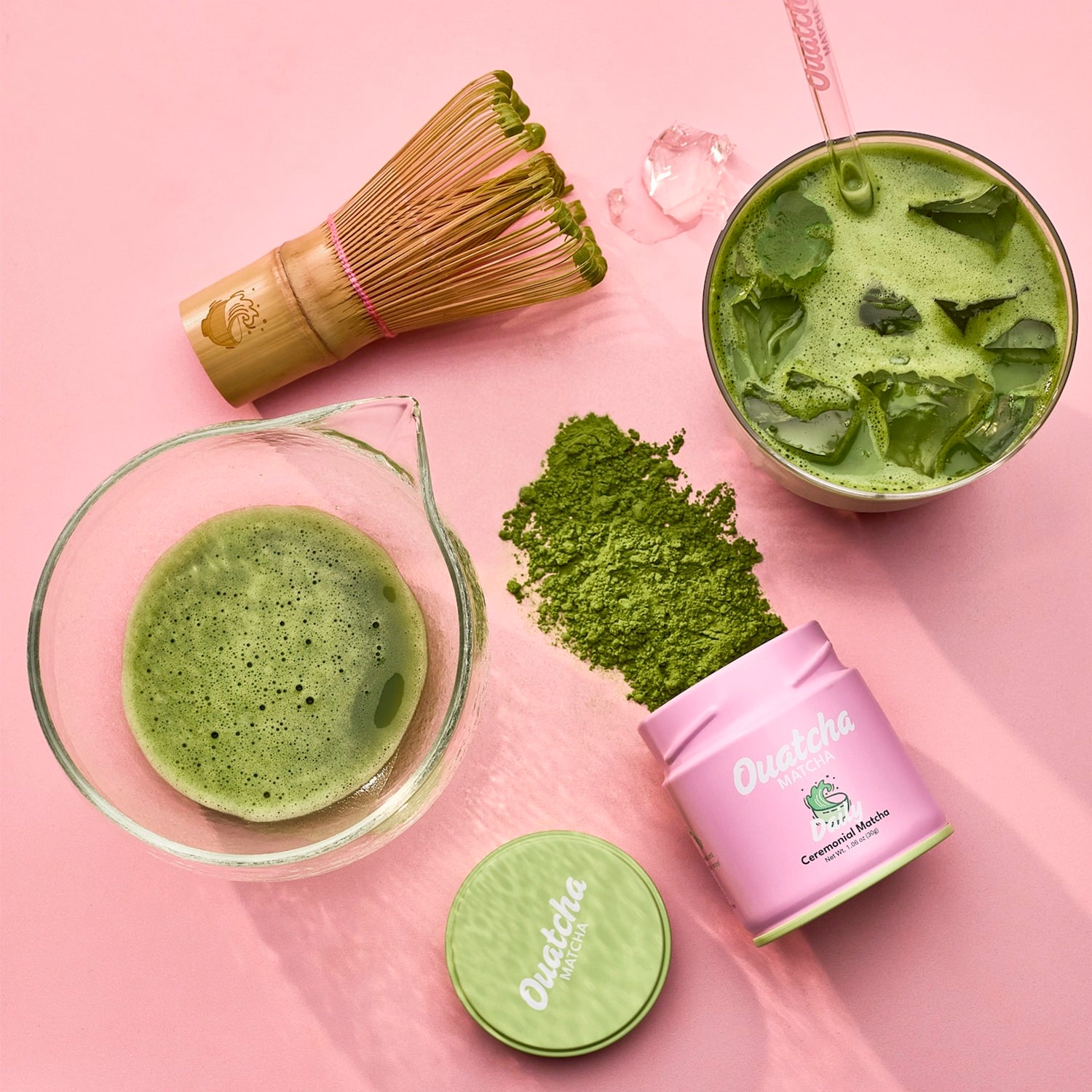 Flat lay of prepared matcha, bamboo whisk, and a Daily Ouatcha Matcha ceremonial-grade first harvest matcha tin on a pink background.